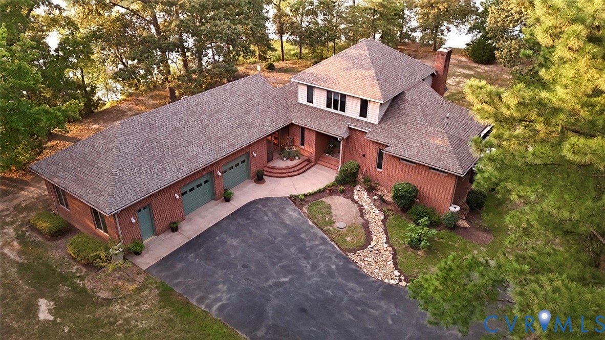 Brick exterior with a multi-level roofline, attached garage, paved drive, and mature trees Brick exterior with a multi-level roofline, attached garage, paved drive, and mature trees