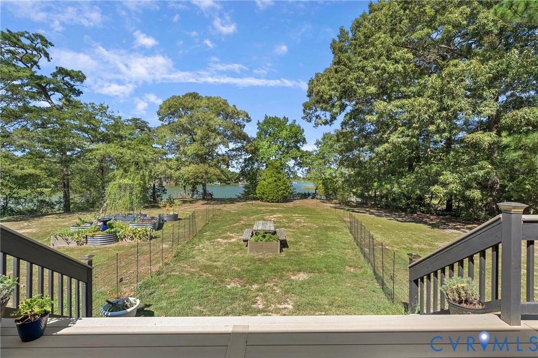 Expansive backyard featuring a sloped lawn, mature trees, and a water backdrop