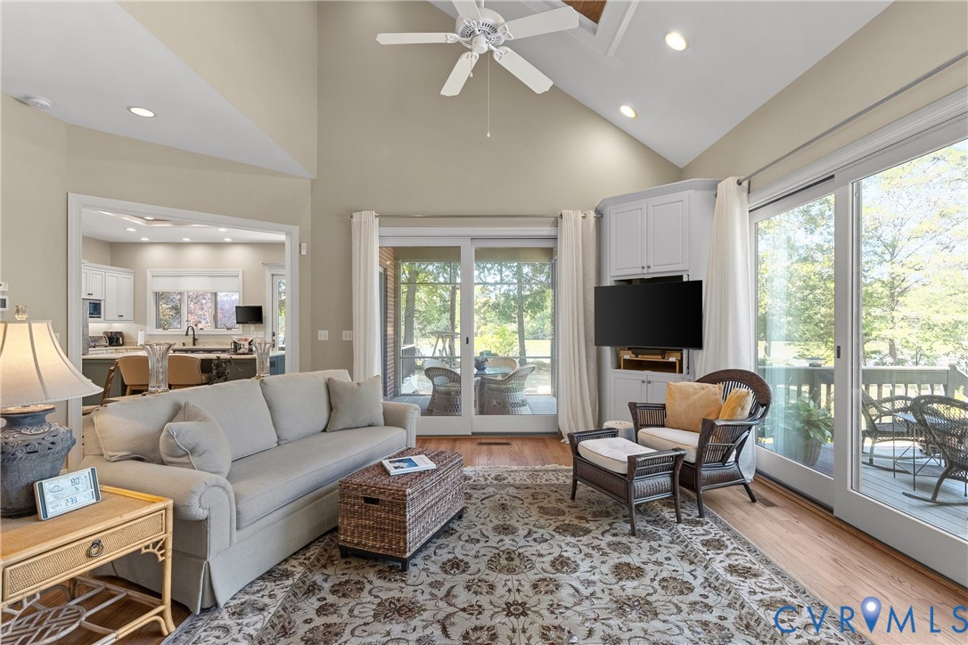 Vaulted ceiling with a ceiling fan, recessed lighting, wood-finish flooring, built-in cabinetry, and sliding glass doors leading to an exterior deck