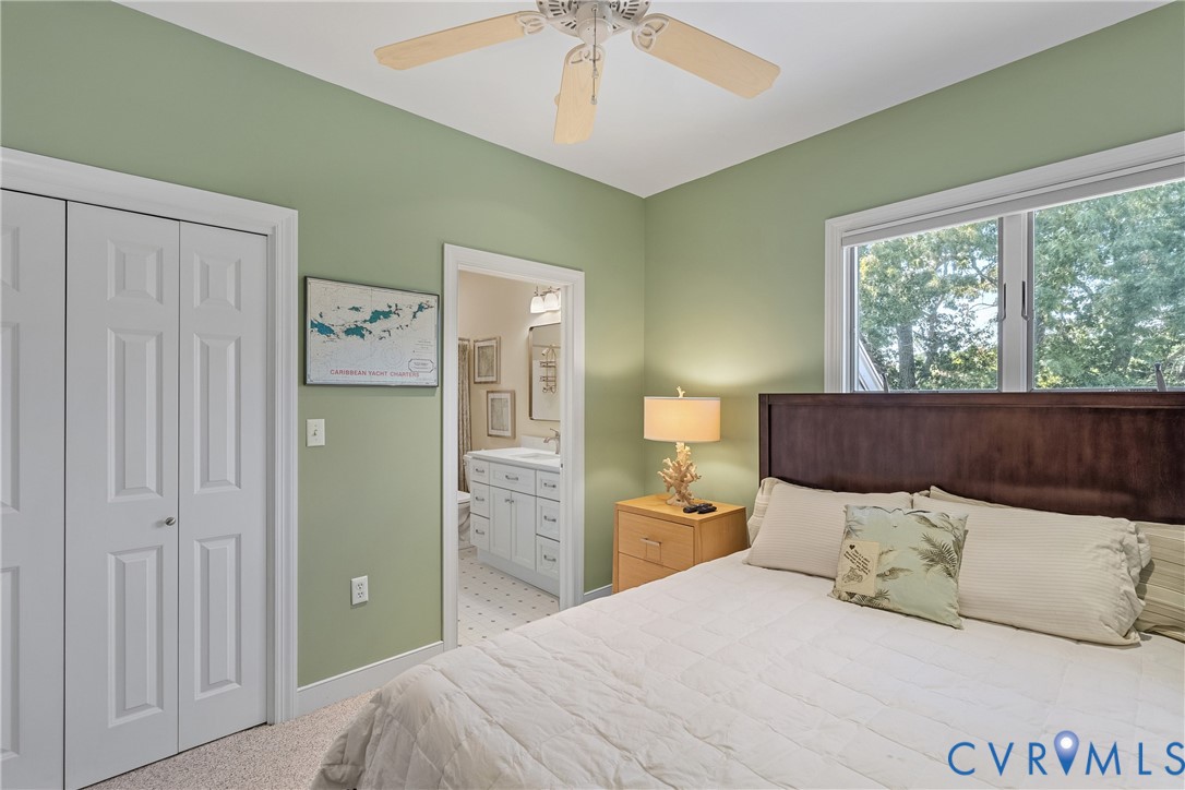Light green walls with white trim, a ceiling fan, a window, and an adjacent bathroom with a white vanity