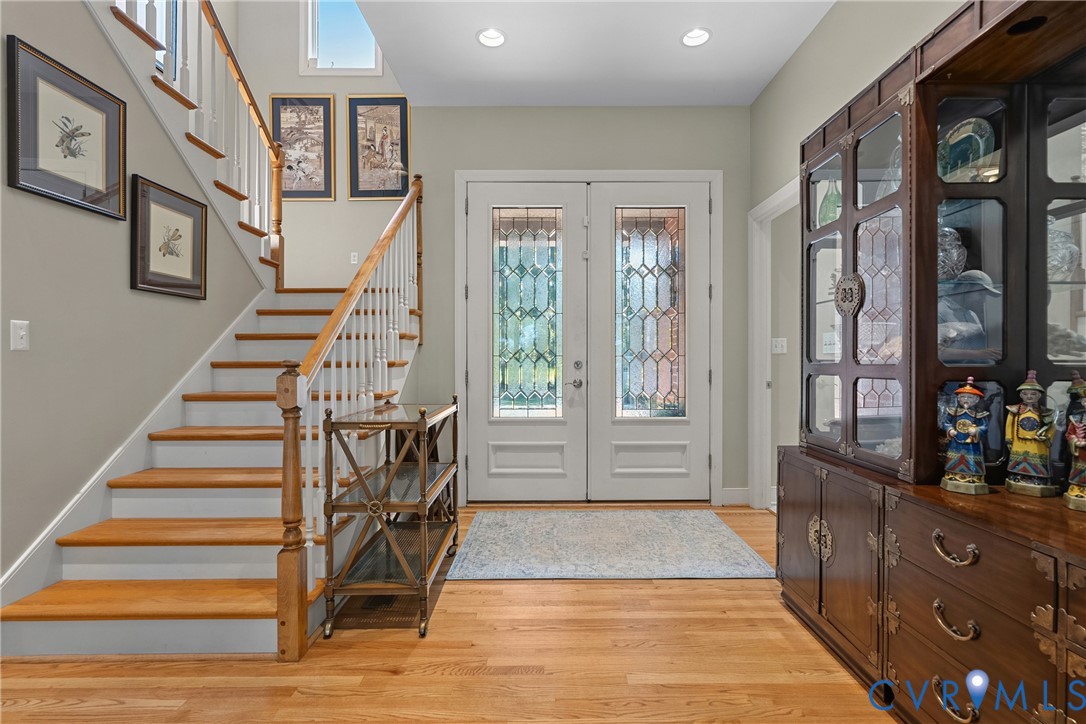 Hardwood flooring, painted white staircase with wood handrail, double entry doors with decorative glass, recessed lighting, and upper transom windows