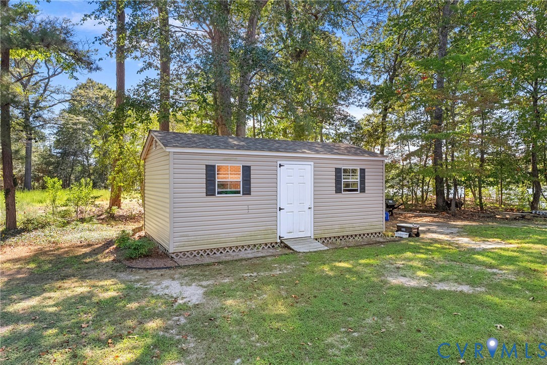 Exterior storage shed with vinyl siding, white paneled door, two windows with shutters, and a wood ramp