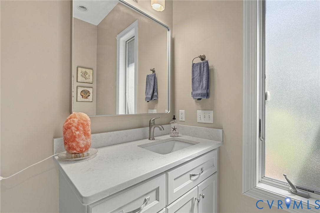 White vanity with recessed panel cabinet doors, brushed nickel hardware, integrated sink, and light-toned countertop