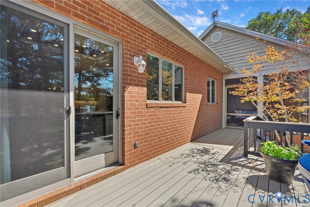 Brick exterior with multiple windows, sliding glass door, composite decking, and a screened porch