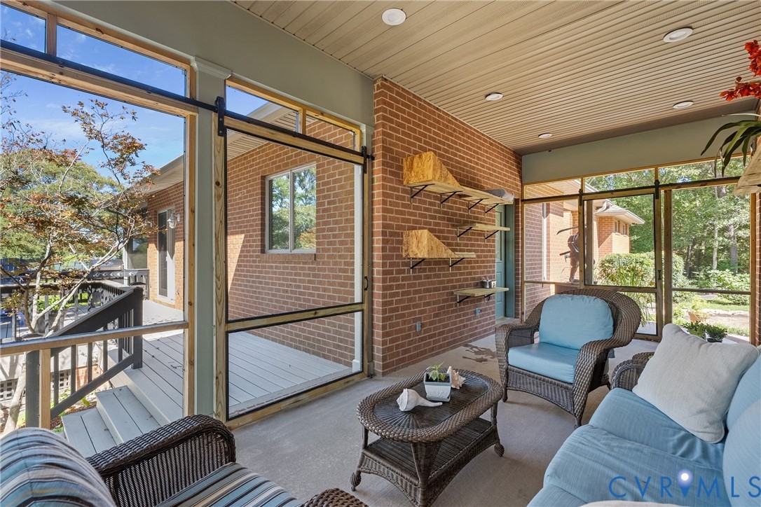 Screened porch with brick wall, recessed lighting, concrete flooring, and sliding screen door