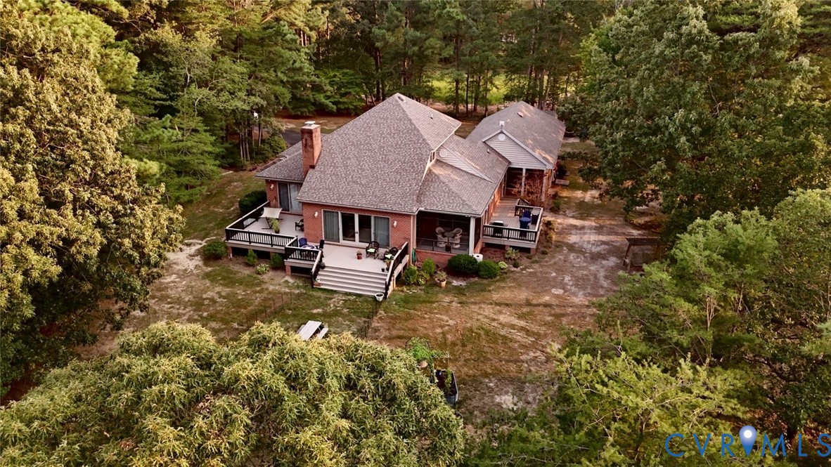 Brick exterior residence with multi-level decks, mature tree surroundings, an asphalt driveway, and a covered porch