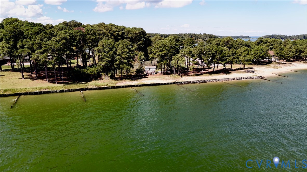 Waterfront property featuring a sandy beach, mature tree canopy, and shoreline protection