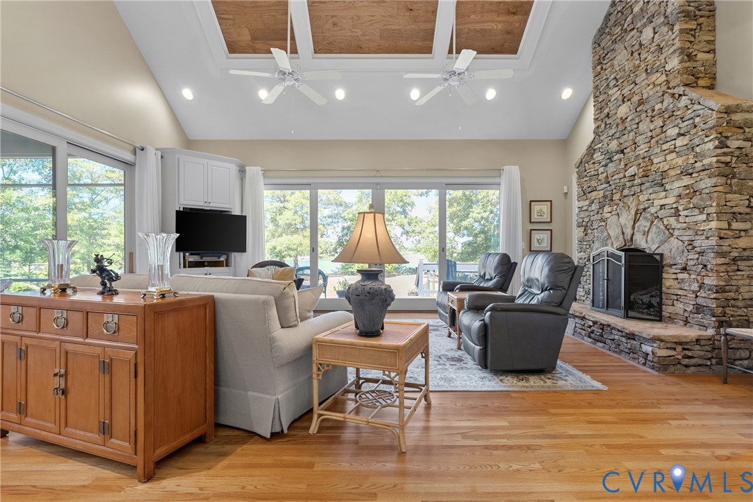 Vaulted ceiling with wood-paneled inserts, recessed lighting, stone fireplace, wood-finish flooring, and expansive glass sliding doors