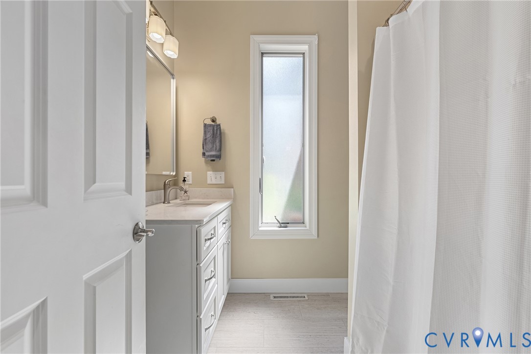 White paneled door, single vanity with light-colored countertop, wall-mounted mirror, brushed nickel faucet, and a frosted vertical window