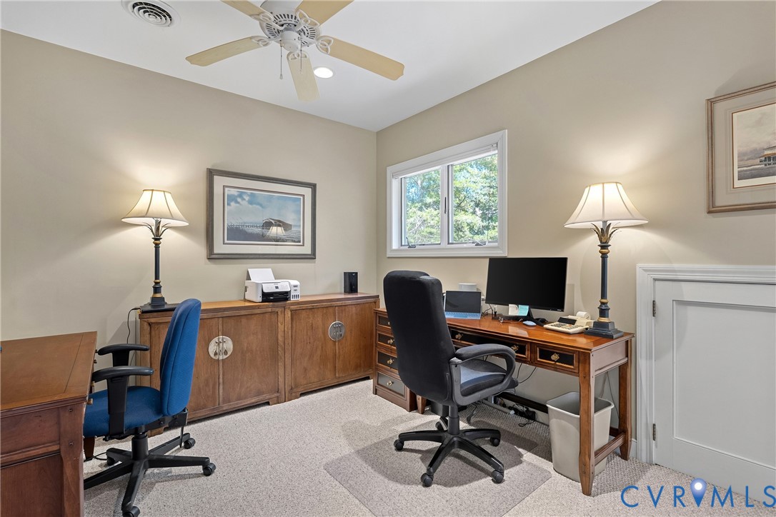 Light-colored wall paint, white trim window, light-toned carpet flooring, ceiling fan with light fixture, and panel door