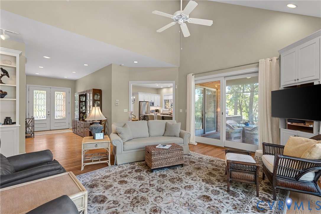 Vaulted ceilings, wood-finish flooring, sliding glass doors to a covered outdoor area, built-in shelving, and a ceiling fan