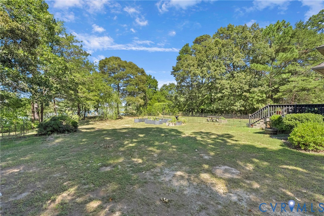 Expansive lawn area with mature trees, a raised garden bed, and a wooden deck with stairs