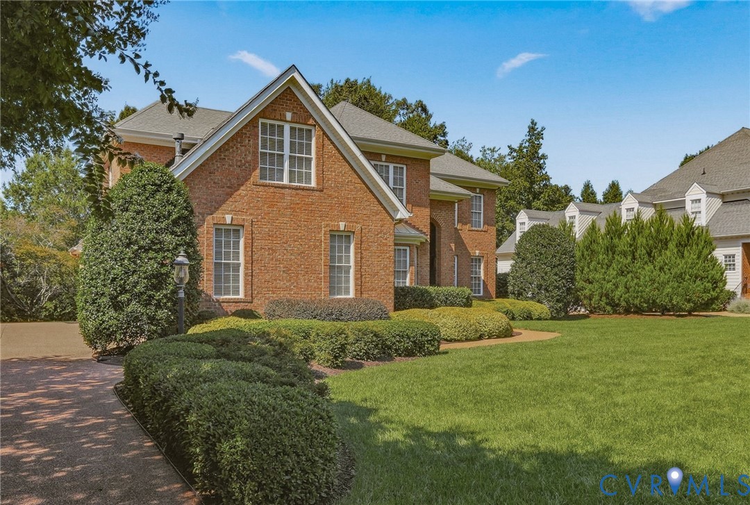 Brick exterior with a gabled roofline, mature trees, and manicured landscaping