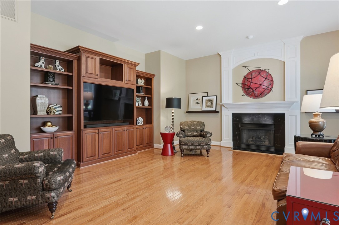 Light wood-finish flooring throughout, built-in entertainment center with shelving, fireplace with dark stone surround, and white decorative mantel