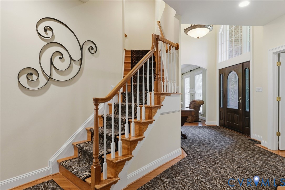 Two-story foyer featuring a wood staircase with white balusters, transom windows, a dark wood-finish entry door with decorative glass, and a semi-flush mount ceiling fixture Two-story foyer featuring a wood staircase with white balusters, transom windows, a dark wood-finish entry door with decorative glass, and a semi-flush mount ceiling fixture