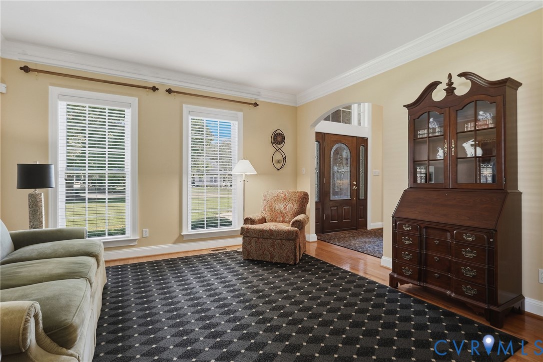 Arched entry with a wood door, wood-finish flooring, two large windows, and crown molding