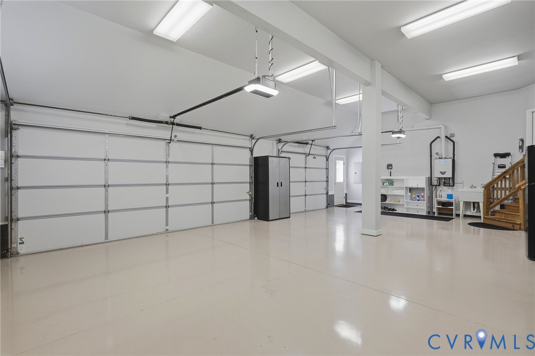 Expansive garage featuring multiple automatic overhead doors, a utility sink, and wood-finish stairs