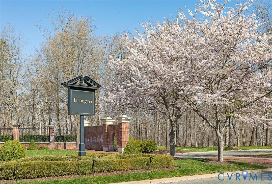 Tarrington community signage with brick and wrought iron fencing, manicured shrubbery, and mature flowering trees