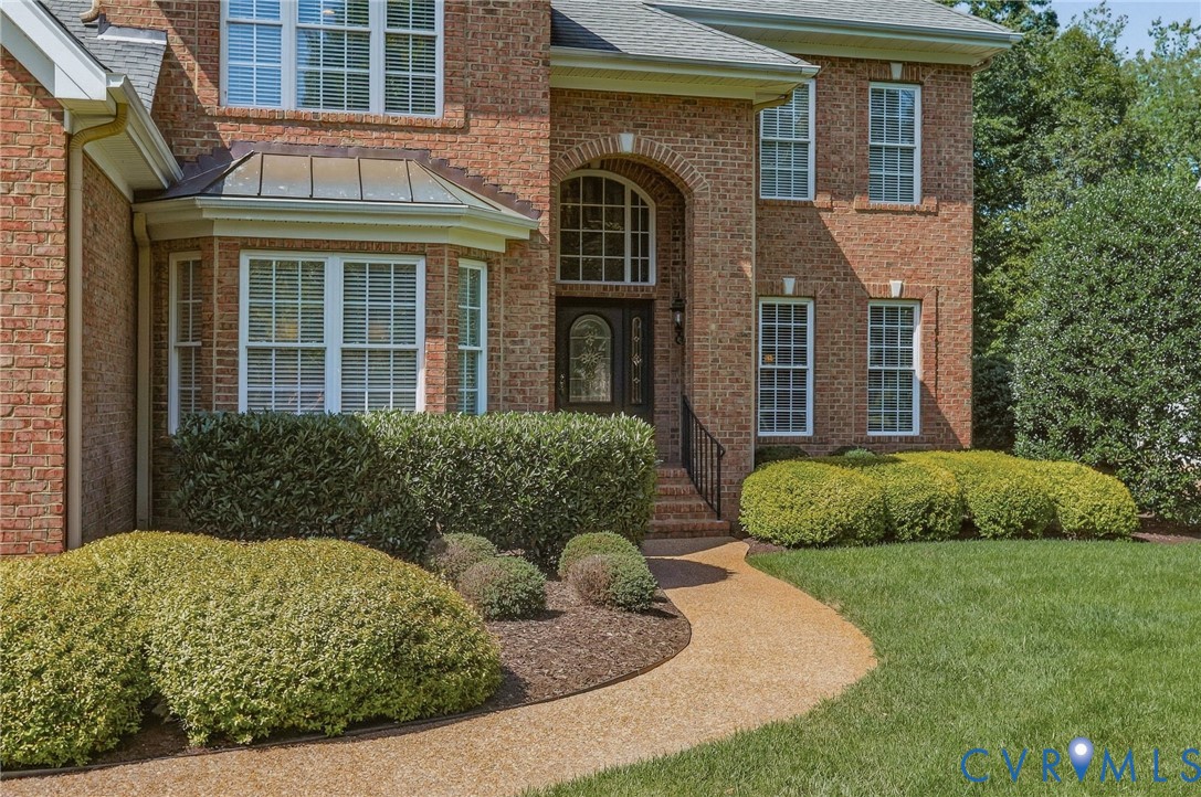 Brick exterior featuring a bay window with a metal roof accent, an arched entryway, a stone pathway, and mature landscaping Brick exterior featuring a bay window with a metal roof accent, an arched entryway, a stone pathway, and mature landscaping