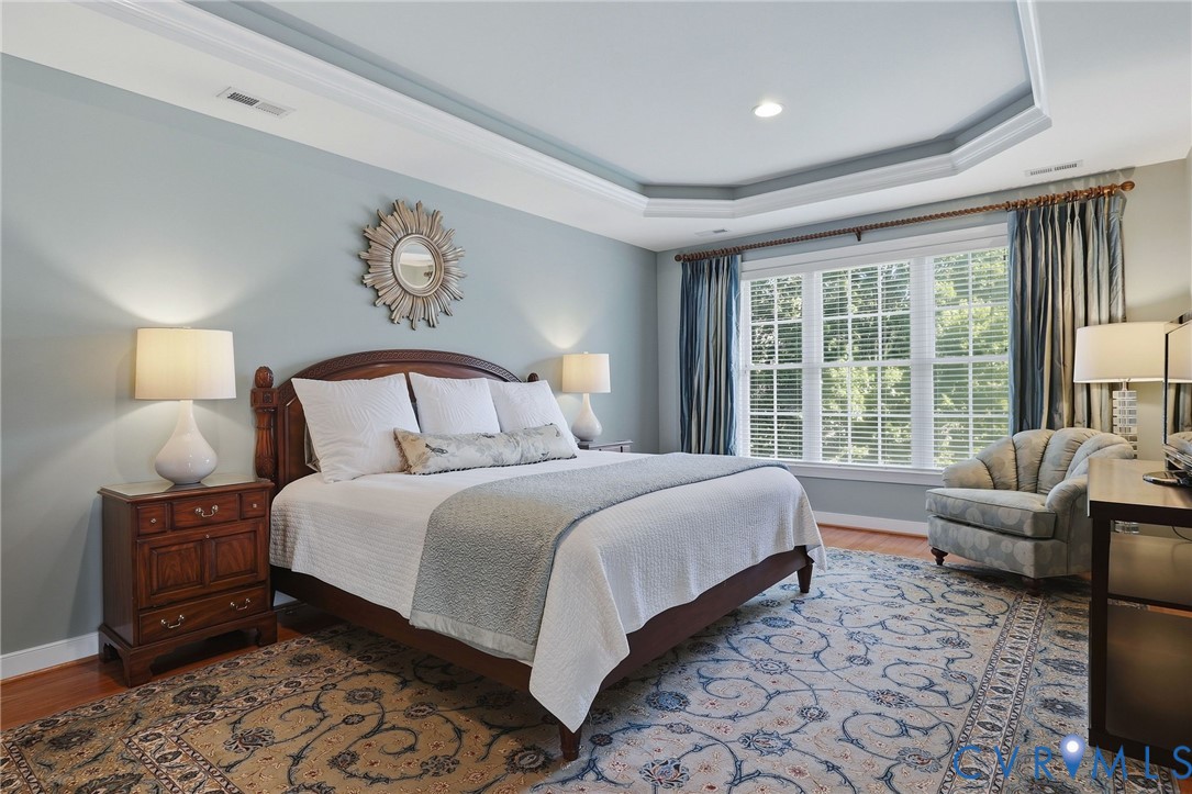 Tray ceiling with recessed lighting, large window with plantation blinds, wood-finish flooring, and a substantial wood bed frame