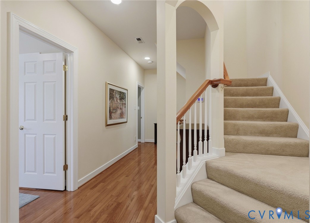 Hallway featuring wood-finish flooring, recessed lighting, and a staircase with carpeted treads, white balusters, and a wood handrail