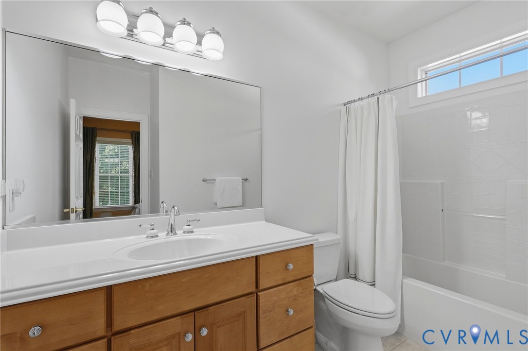 Elongated vanity mirror, four-light fixture, wood-finish cabinetry, integrated sink, and white shower-tub combination