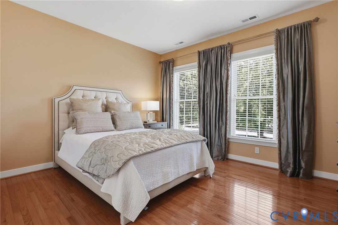 Hardwood flooring, two large windows with blinds, a neutral wall color, and white trim