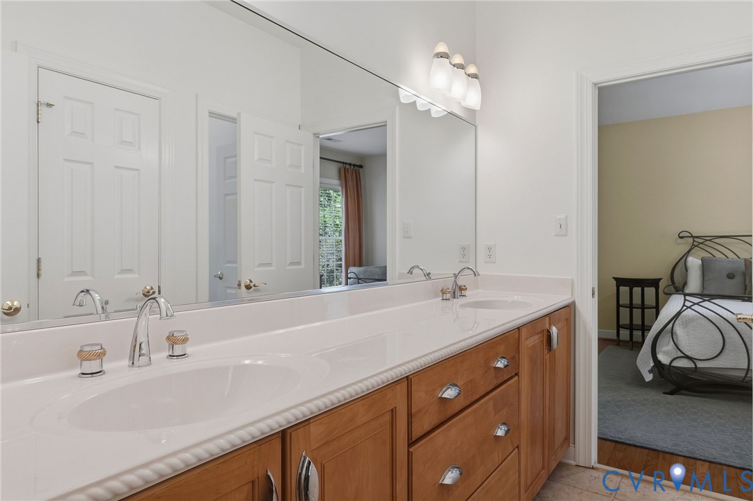 Elongated vanity with dual integrated sinks, chrome fixtures, full-width mirror, and wood-finish cabinetry