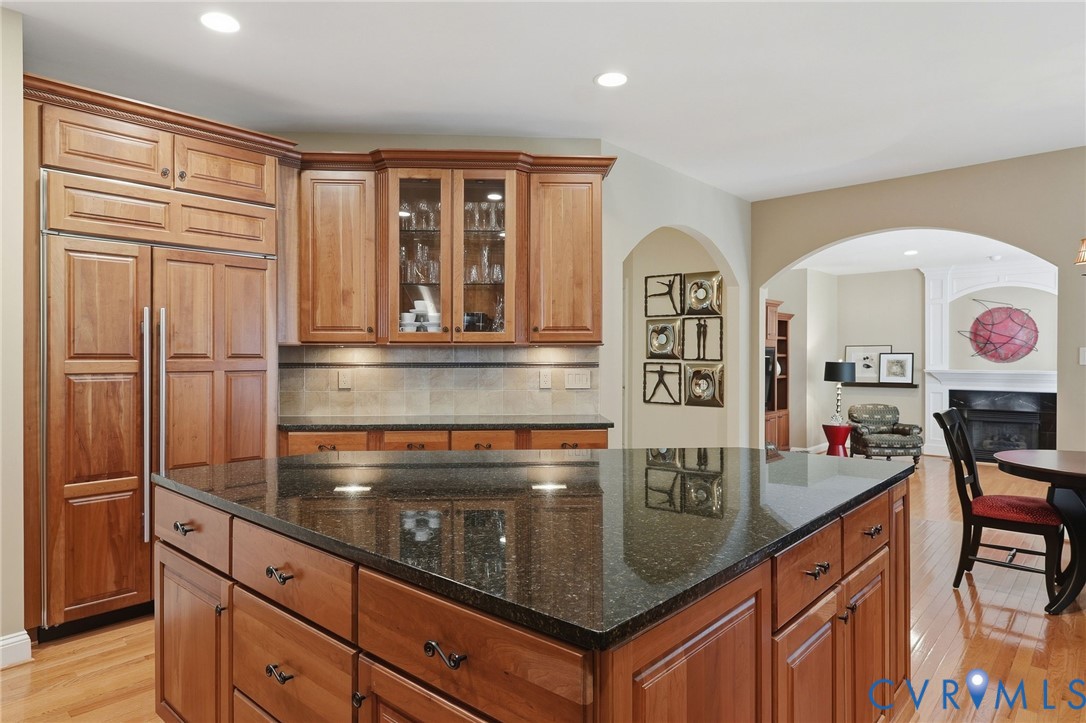 Kitchen featuring wood cabinetry, a large kitchen island with a dark countertop, paneled built-in refrigerator, and wood-finish flooring