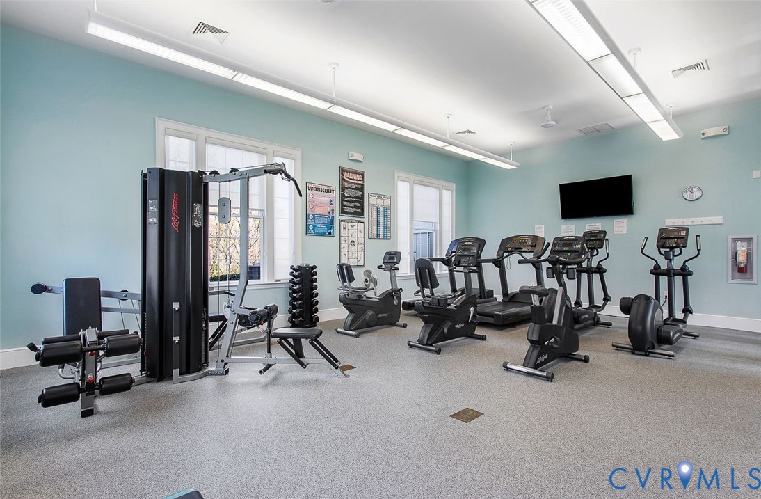 Dedicated fitness center featuring multiple cardio machines, strength training equipment, a wall-mounted television, and ample natural light