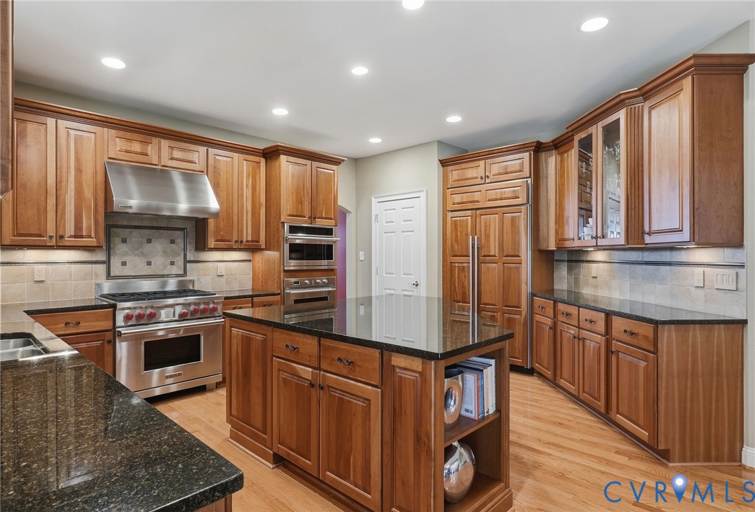 Wood-finish cabinetry with crown molding, stainless steel appliances, dark stone countertops, tile backsplash, and recessed lighting Wood-finish cabinetry with crown molding, stainless steel appliances, dark stone countertops, tile backsplash, and recessed lighting