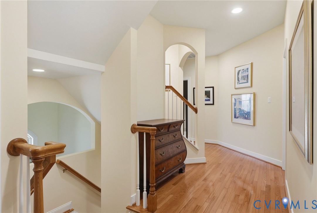 Archway entry, recessed lighting, wood-finish flooring, white balusters, and wood handrails