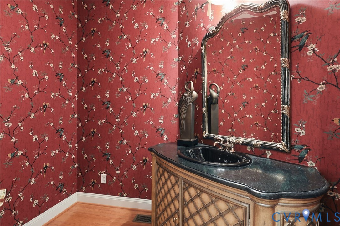 Red patterned wallpaper, ornate mirror, black basin sink, dark countertop, and wood-finish vanity