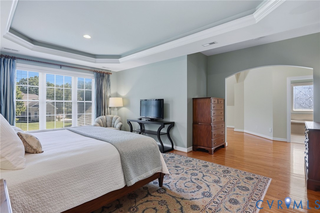 Tray ceiling with recessed lighting, large window with ample natural light, wood-finish flooring, and arched doorway
