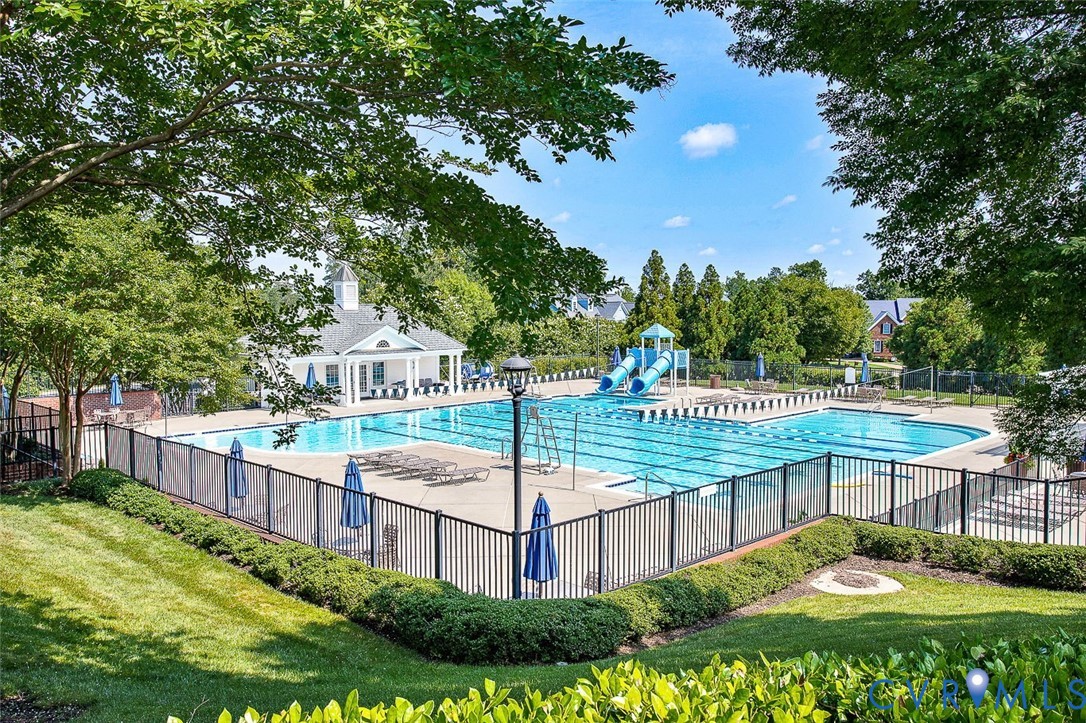 Expansive community pool with multiple swimming lanes, two water slides, a dedicated wading area, and a clubhouse