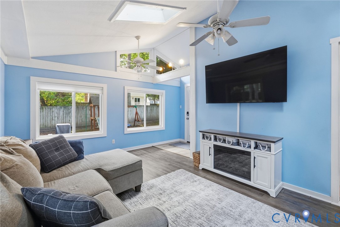 Vaulted ceiling with skylight, wood-finish flooring, multiple windows, and a built-in media console with an electric fireplace