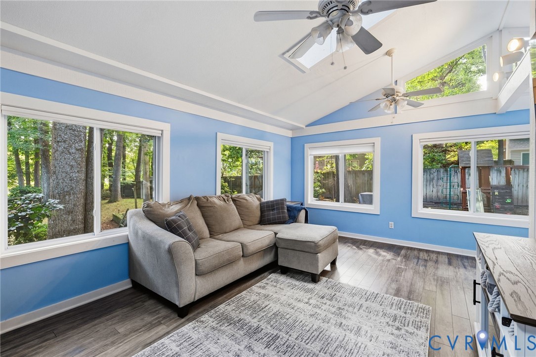 Vaulted ceiling with exposed beams, multiple windows, wood-finish flooring, and a ceiling fan