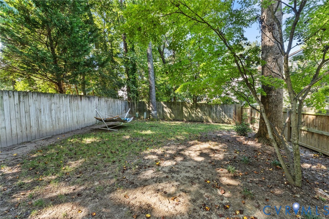 Expansive backyard featuring mature trees and a wood fence perimeter