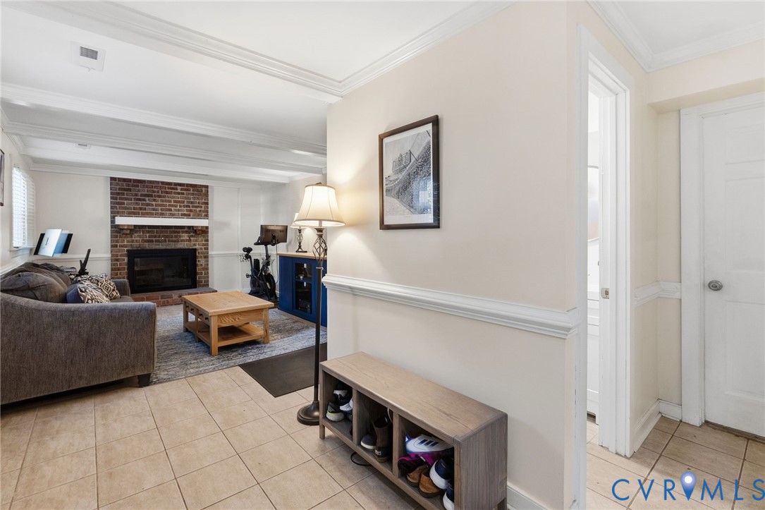 Brick fireplace with a white mantel, ceiling beams, crown molding, and tiled flooring