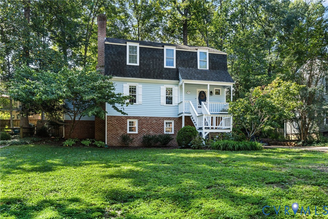 Two-story exterior with light blue siding, brick foundation, dormer windows, and a covered porch with white railings
