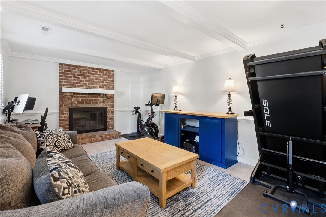 Brick fireplace with a white mantel, light-toned wood-finish flooring, and white ceiling with decorative beams