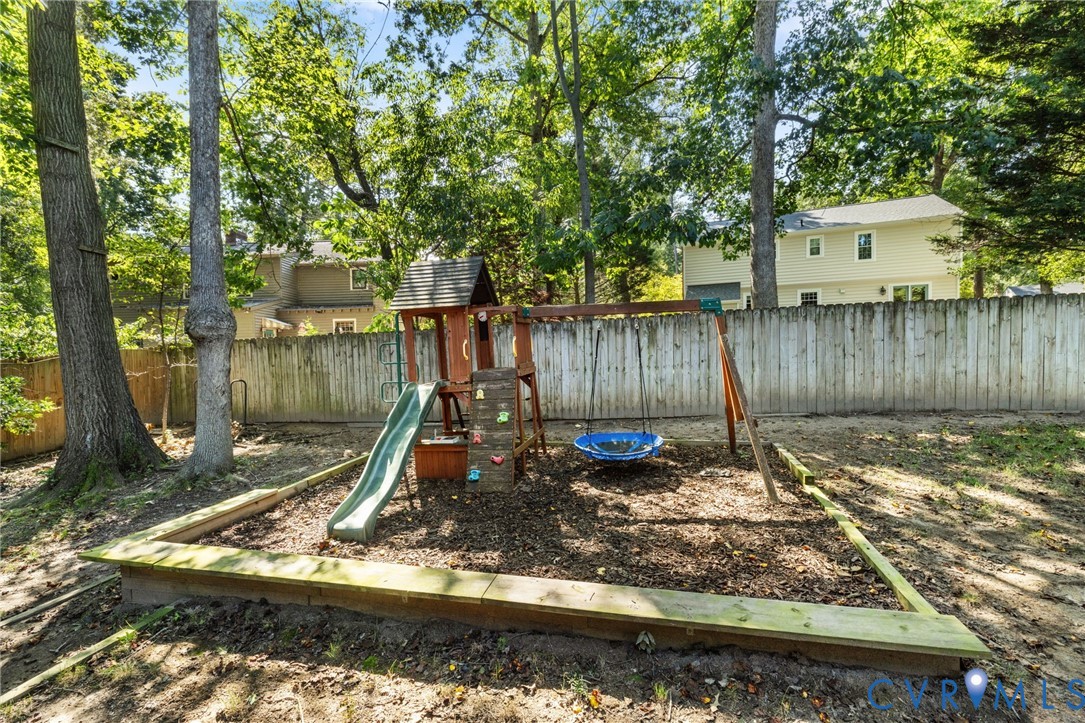 Wood-fenced backyard with mature trees and a dedicated play area featuring a slide and swing set