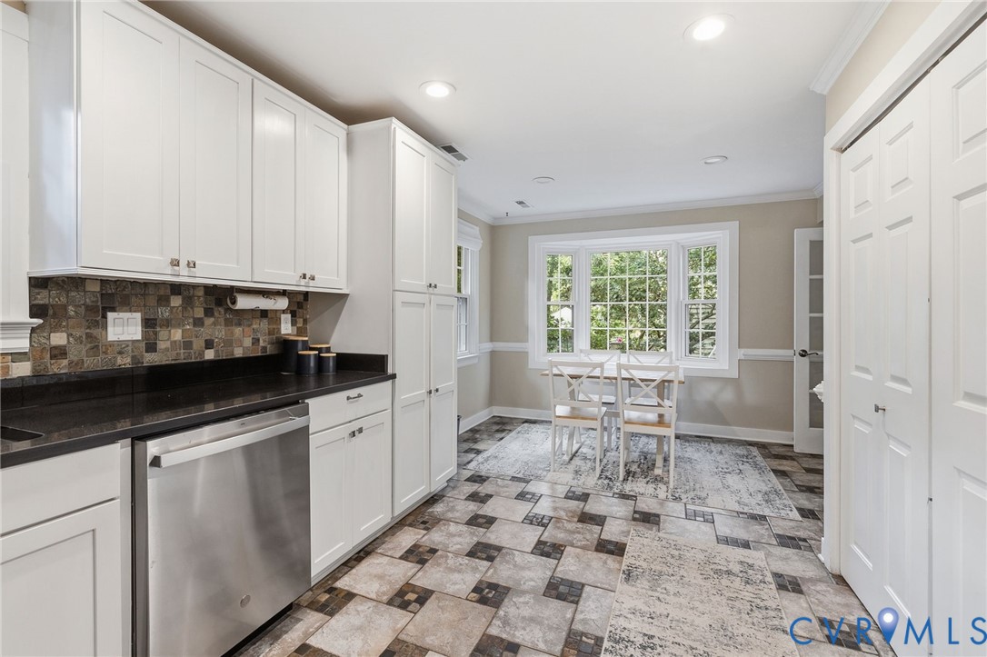 White shaker-style cabinetry, dark countertops, built-in stainless steel dishwasher, tile backsplash, and a multi-pane window