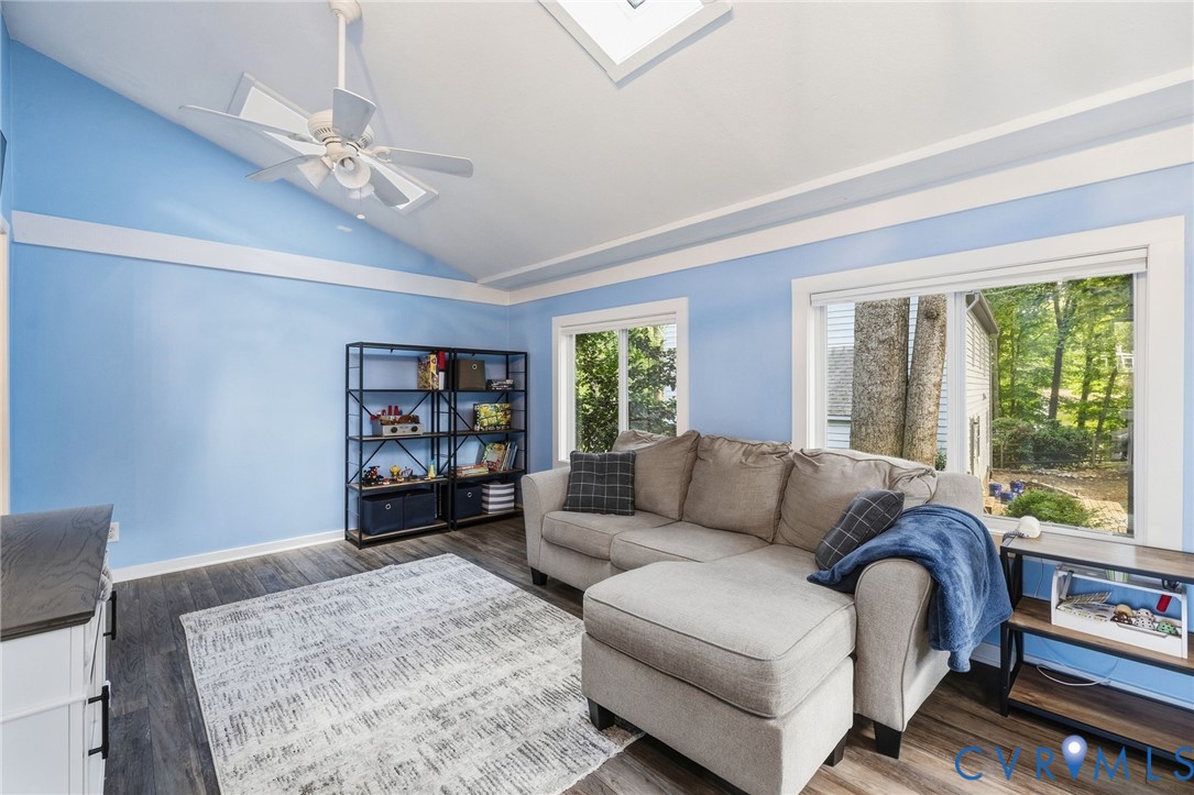 Vaulted ceiling with a ceiling fan, skylight, wood-finish flooring, built-in shelving, and multiple windows
