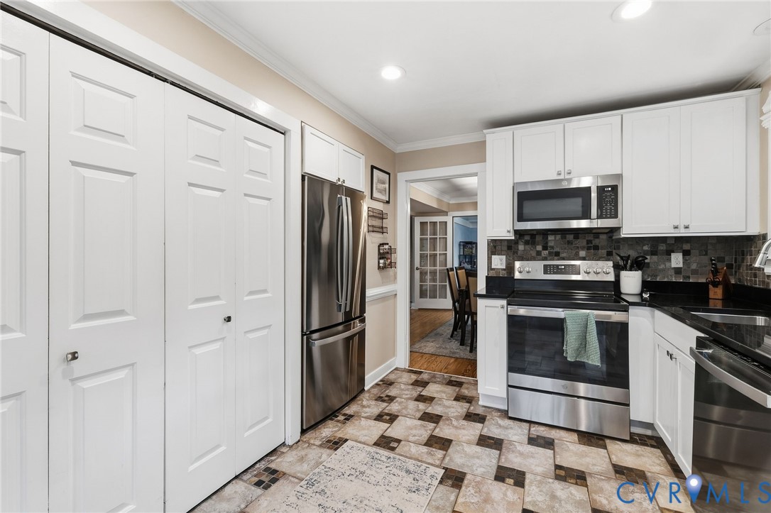 White cabinetry, stainless steel appliances, black countertops, tile backsplash, and patterned floor tile