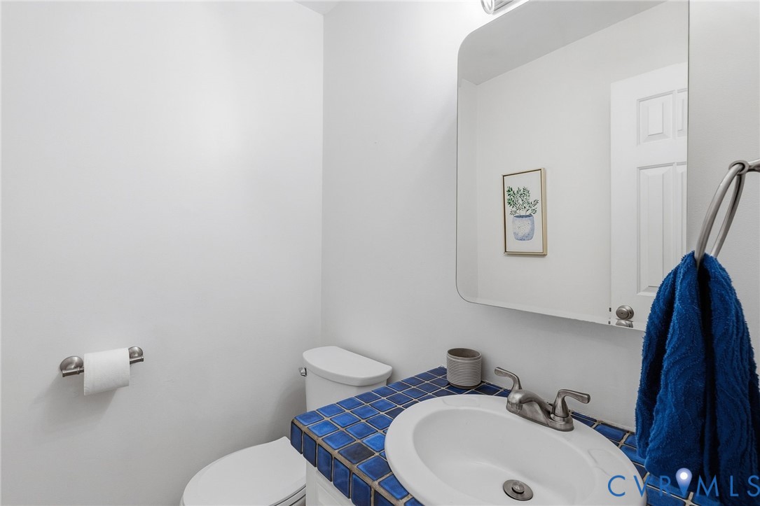White walls with a wall-mounted paper holder, toilet, and a sink with a blue tiled countertop