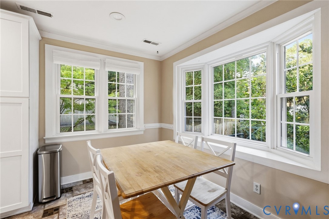 White cabinetry, crown molding, wall paneling, and a large bay window with multiple panes