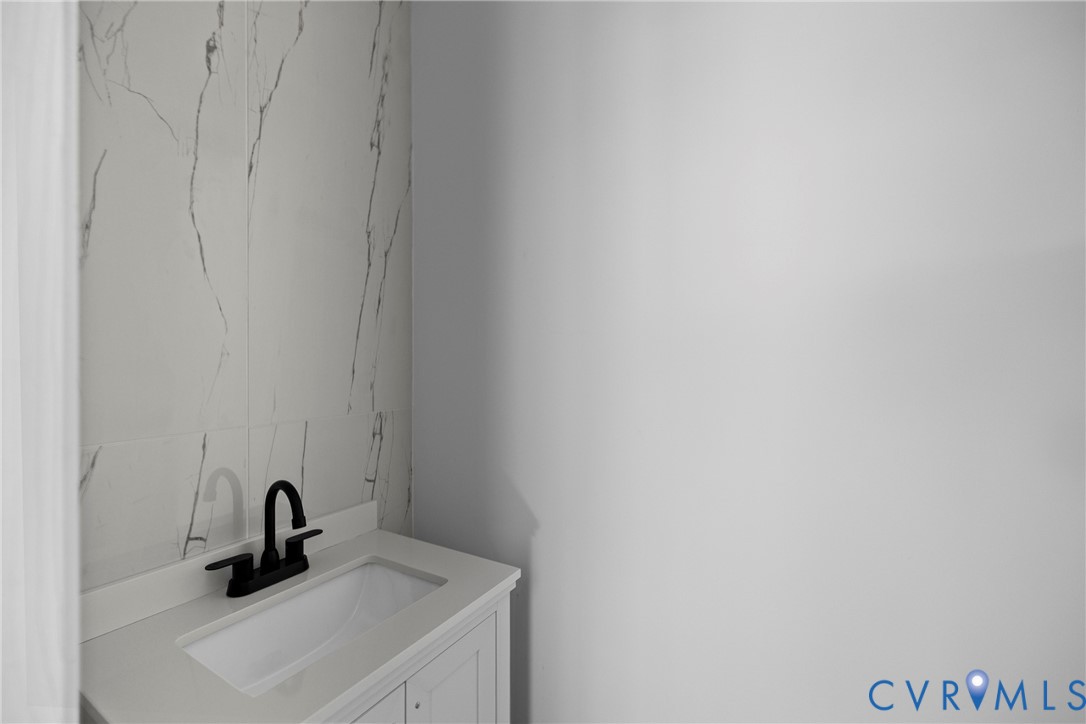 White vanity with an integrated sink, matte black faucet, and a large format tiled accent wall