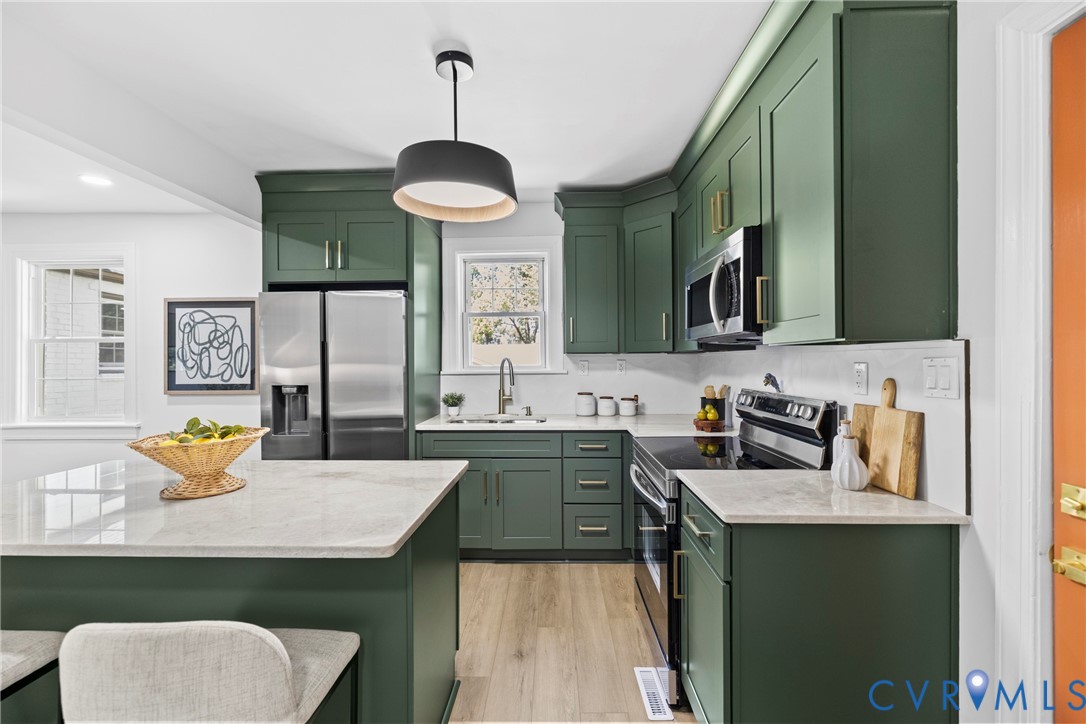 Kitchen featuring green cabinetry, stainless steel appliances, light-toned countertops, wood-finish flooring, and a contemporary pendant light fixture