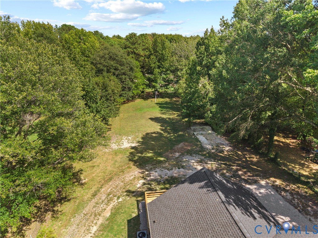 Expansive wooded lot with dense tree lines, a grassy clearing, and a partial view of the property's roofline